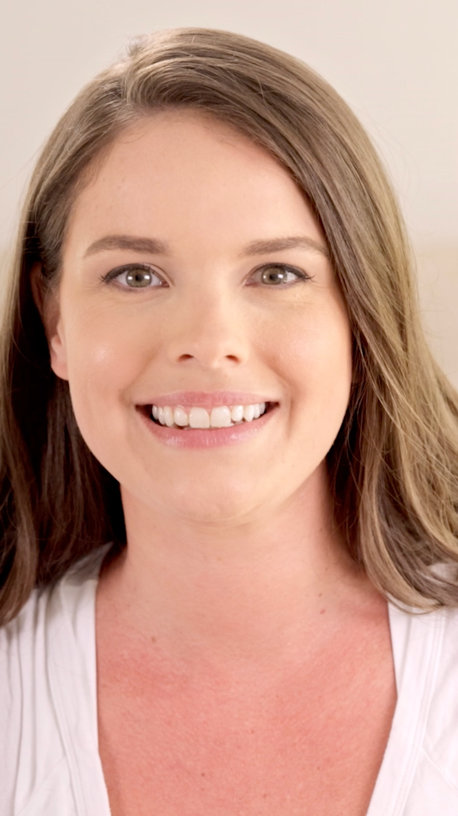Woman with shoulder-length brown hair wearing a white top against a plain background