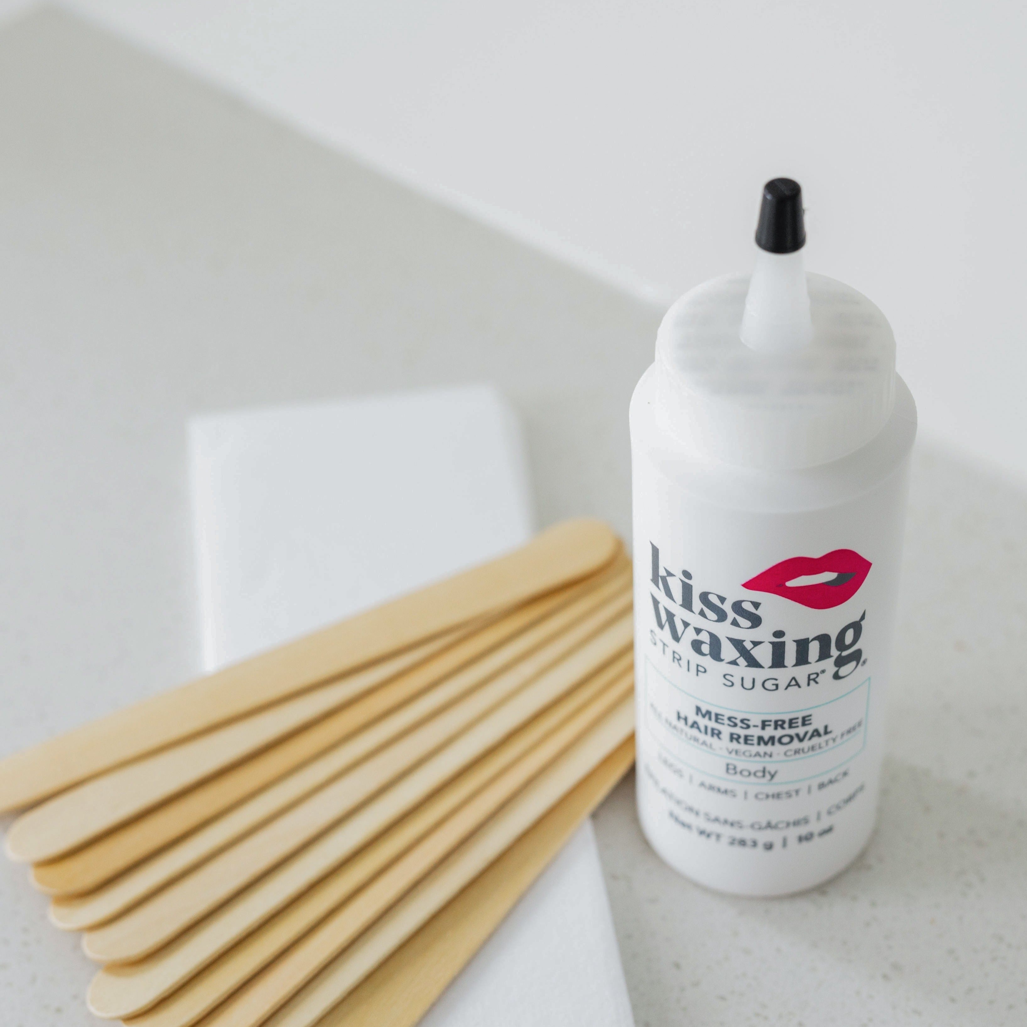 Bottle of kiss waxing strip sugar fine hair with wooden spatulas on a bathroom sink