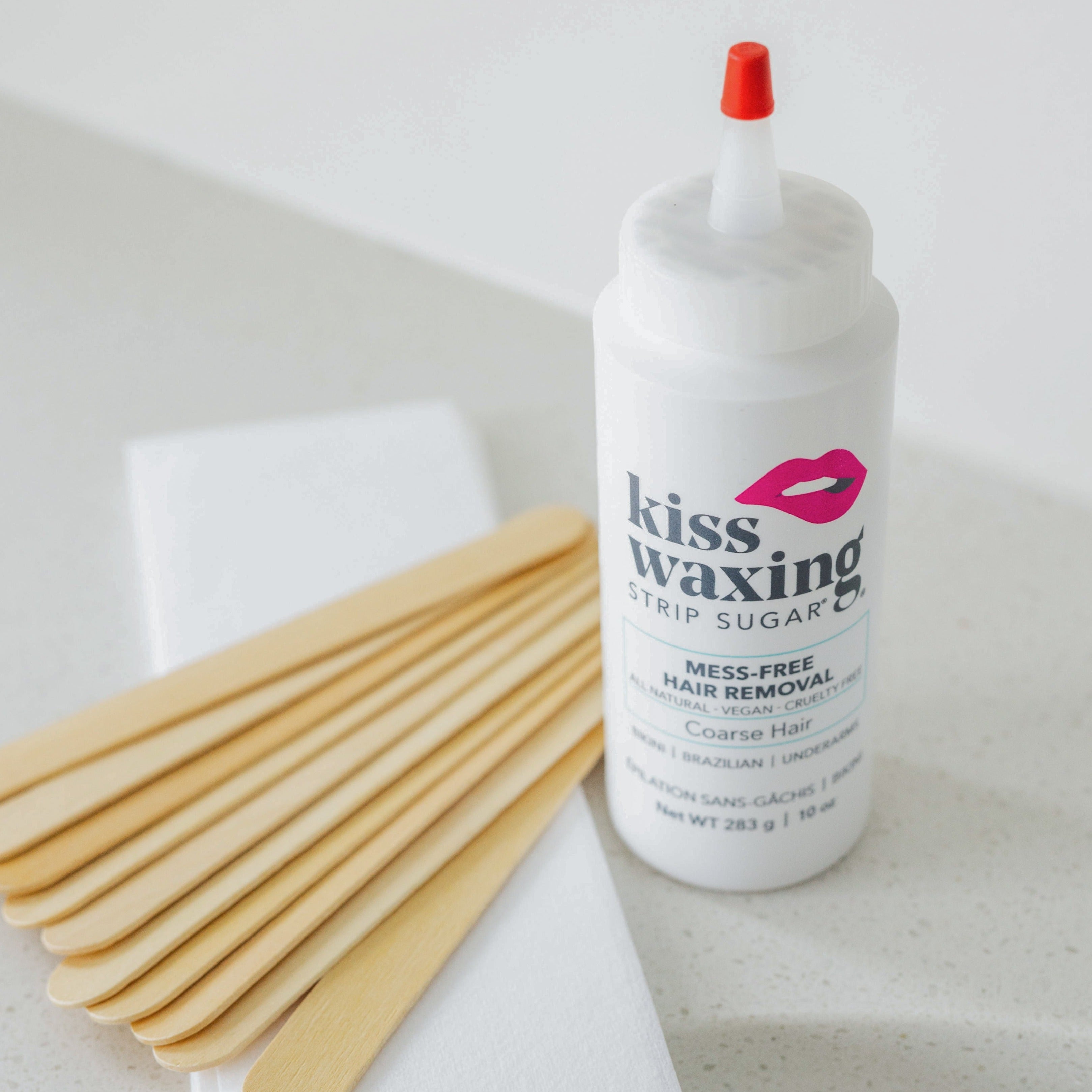 Bottle of kiss waxing strip sugar coarse hair with wooden spatulas on a bathroom sink