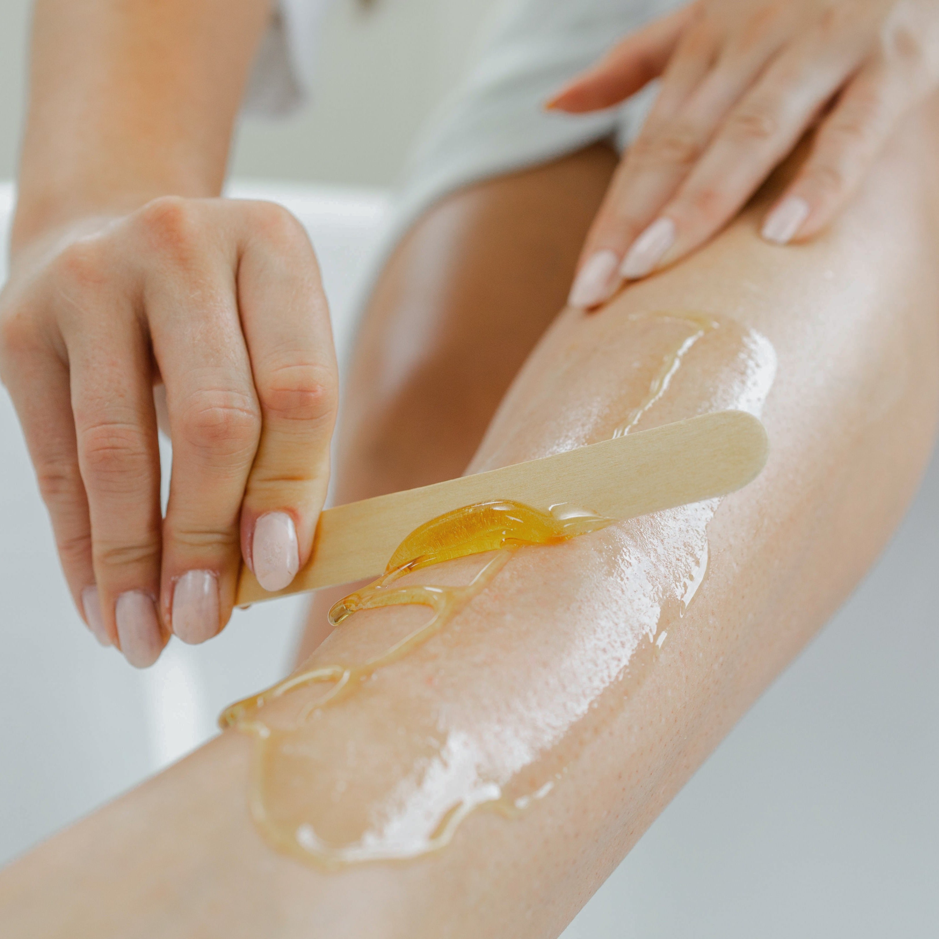 Person applying kiss waxing strip sugar with a wooden spatula on their leg.