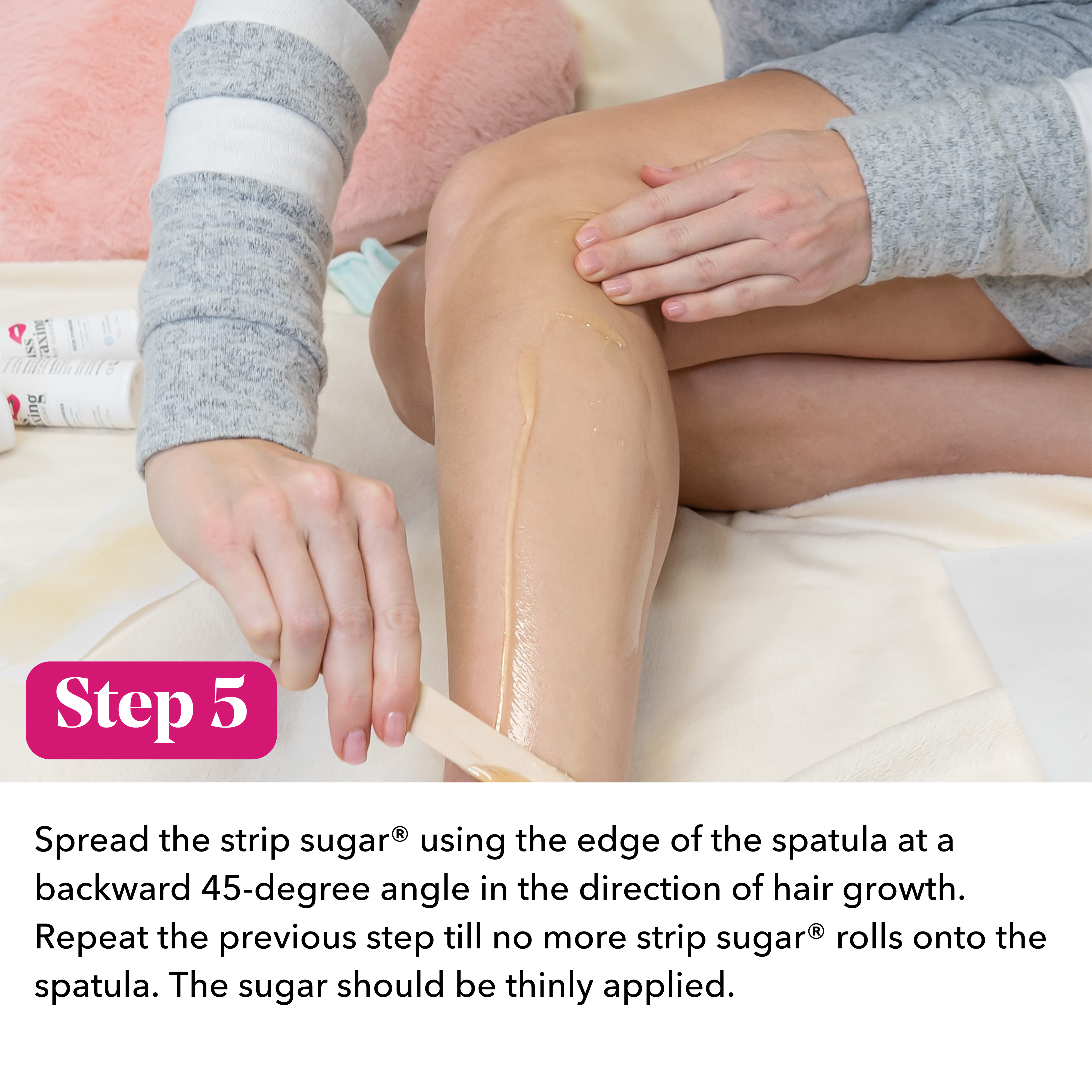 Person applying strip sugar to legs with text instructions saying "Step 5: spread the strip sugar using the edge of the spatula at a backward 45-degree angle in the direction of hair growth. Repeat the previous step till no more strip sugar rolls onto the spatula. The sugar should be thinly applied."